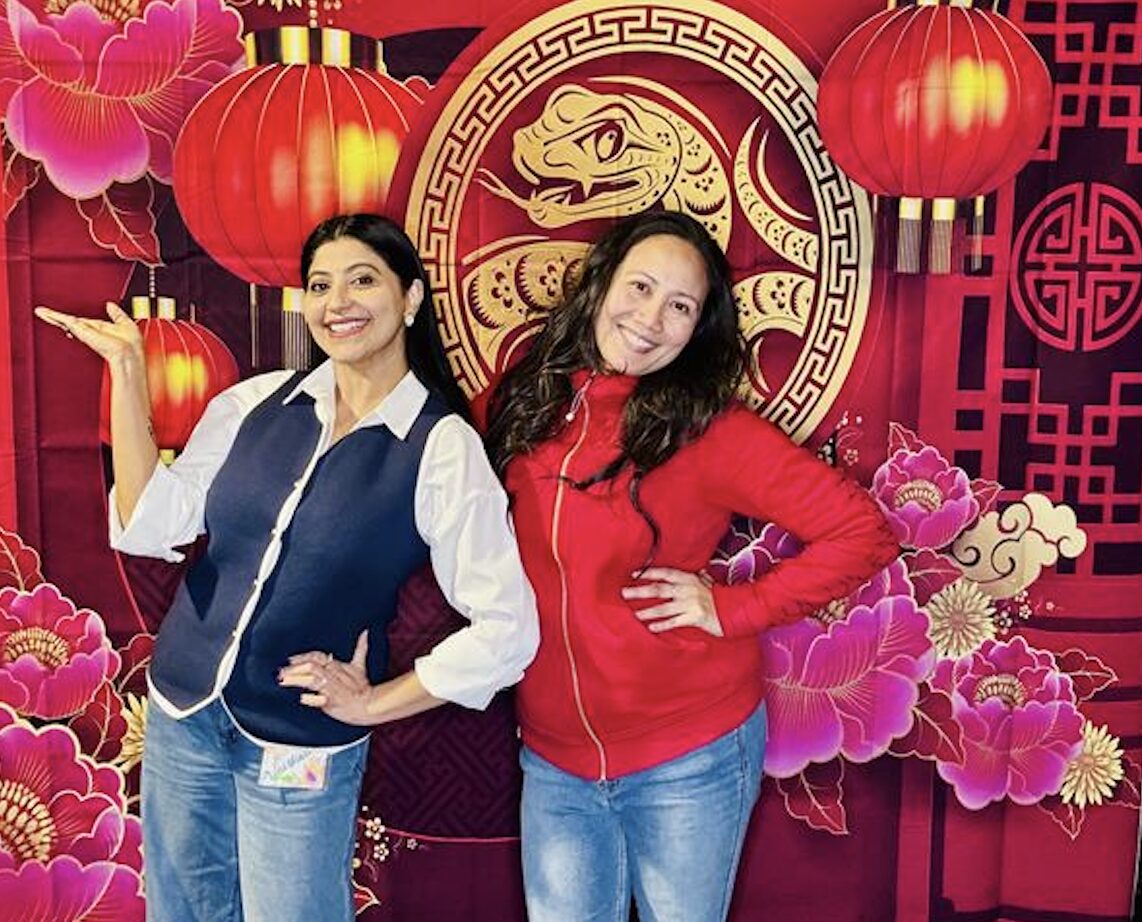 Two women posing in front of a Lunar New Year banner